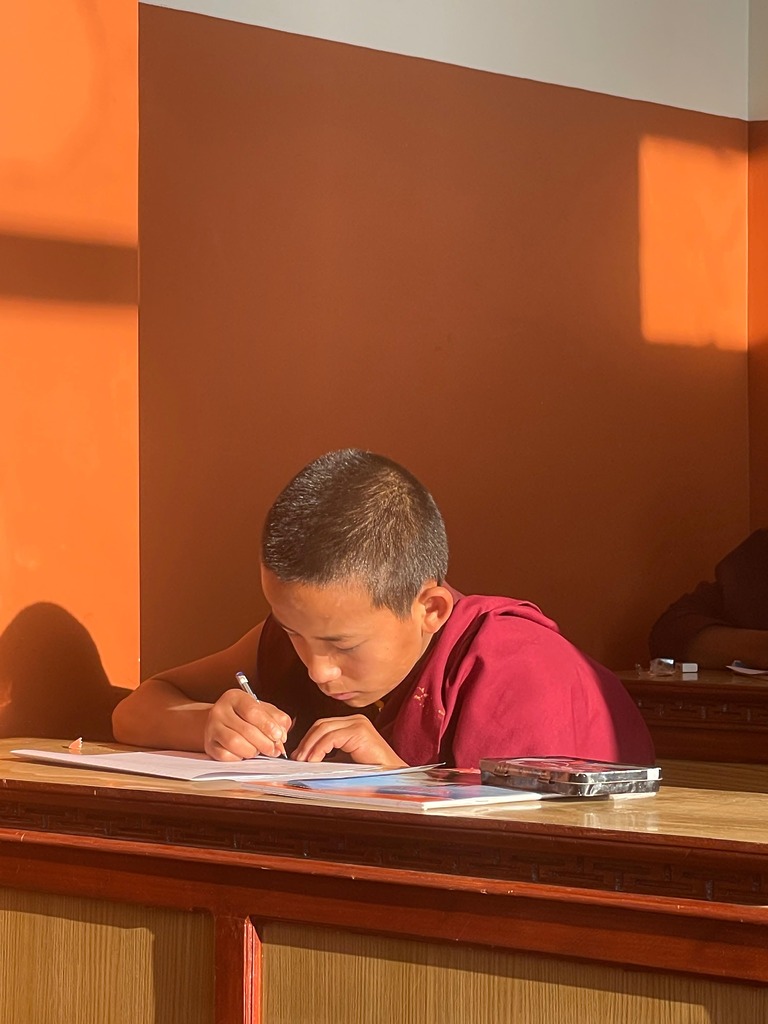 Junger Mönch schreibt konzentriert in ein Heft während des Unterrichts.