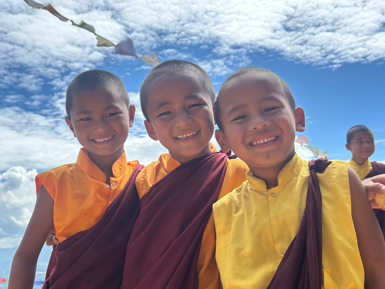 Zwei junge Mönche lachen fröhlich vor blauem Himmel in der Nähe der Klosterschule.