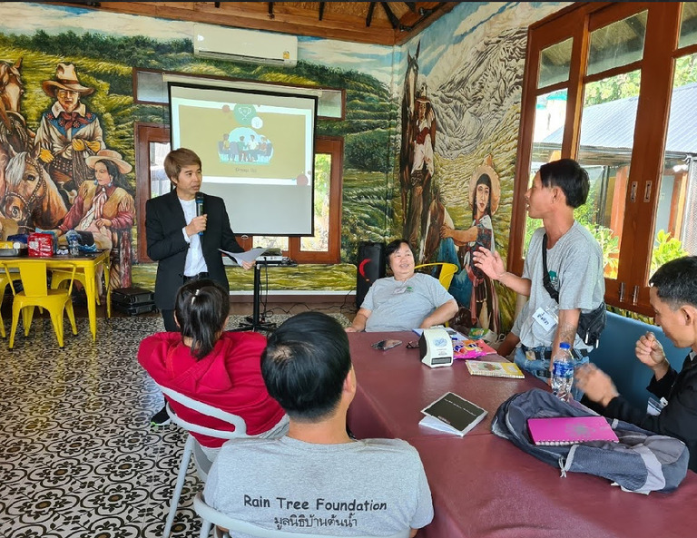 Teilnehmer eines Teamtrainings sitzen in einem offenen Pavillon und hören einer Präsentation zu