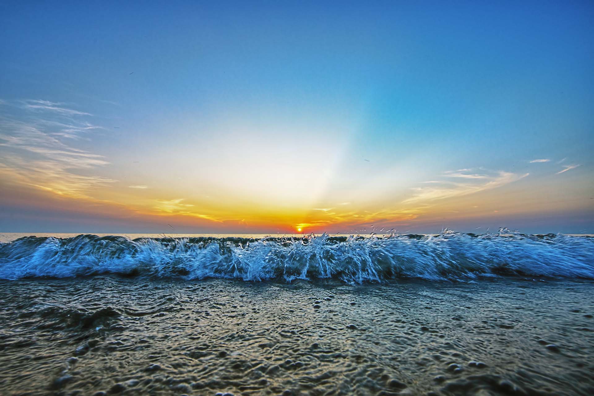 Wave coming to shore at sunset with sunbeams.