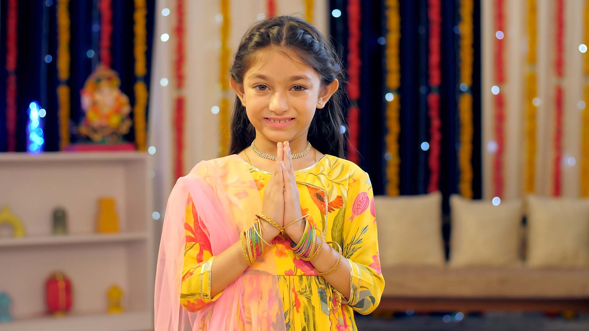 An Indian child greeting in a Indian Namaste pose, colorful background, Diwali decoration , gesture